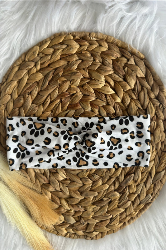 A twist headband with leopard print spots and dog paw prints on a white background. Placed on a wicker photo prop.