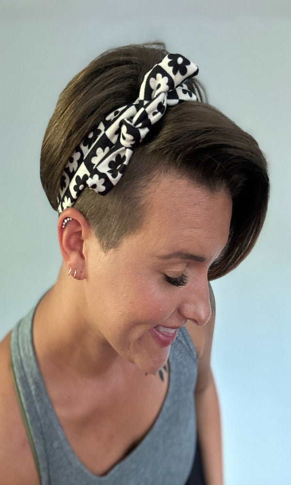 Black and white checkered floral tie headband tied into a bow on a smiling woman with short and half buzzed hair.