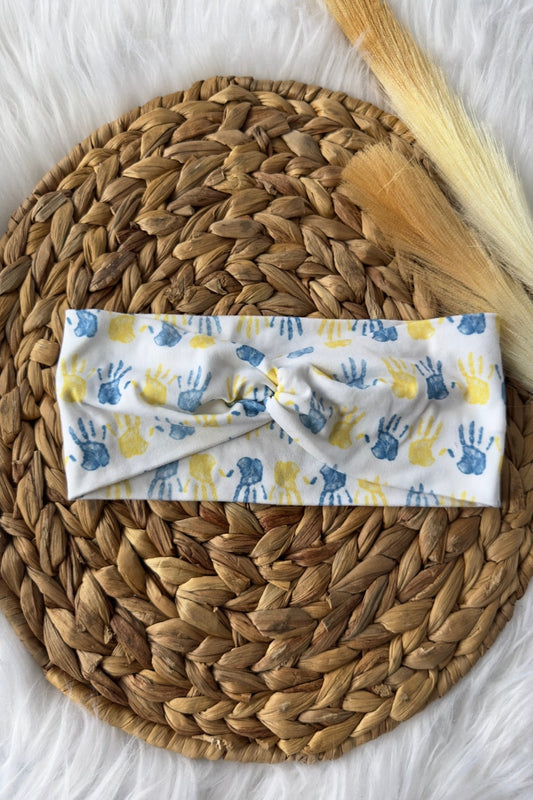 Blue and yellow child handprints on a white headband for down syndrome awareness. Placed on a wicker photo prop.